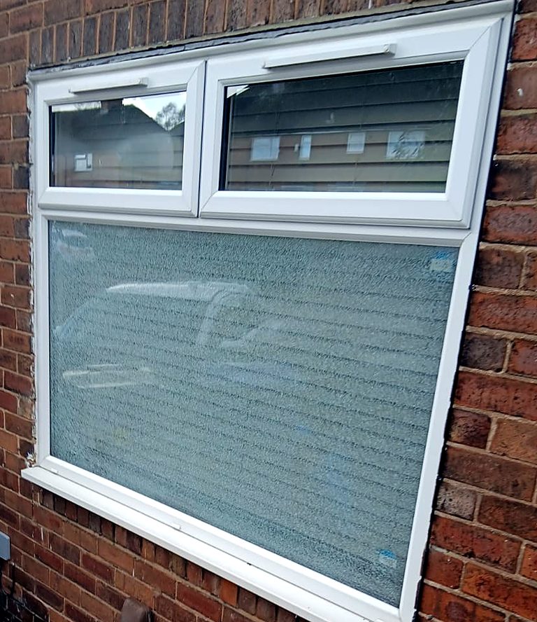 A large pane in a white uPVC window on a brick house, shattered into granules but still standing in the frame