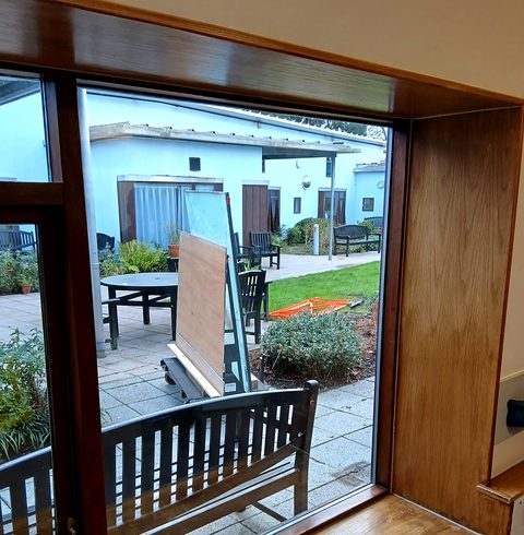 Looking out through a newly glazed timber-framed window onto a courtyard, with the old panes stacked outside