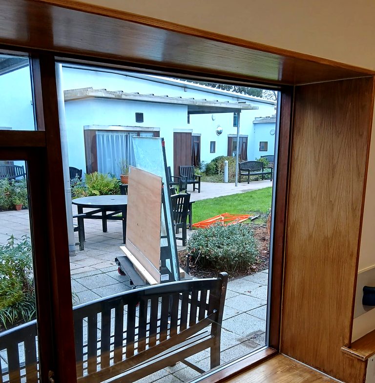 Looking out through a newly glazed timber-framed window onto a courtyard, with the old panes stacked outside