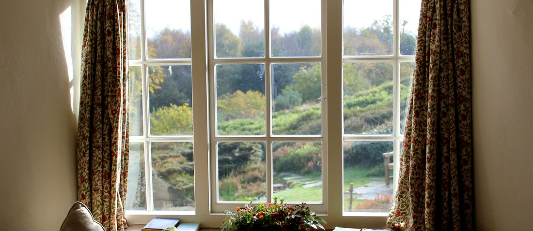 A painted timber window with small panes and glazing bars, looking onto a garden